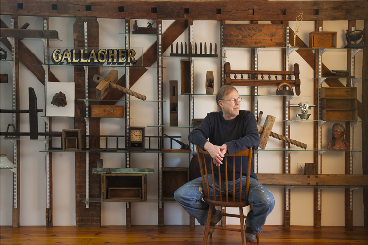 Tim Duff Gallagher seated in front of a studio installation wall